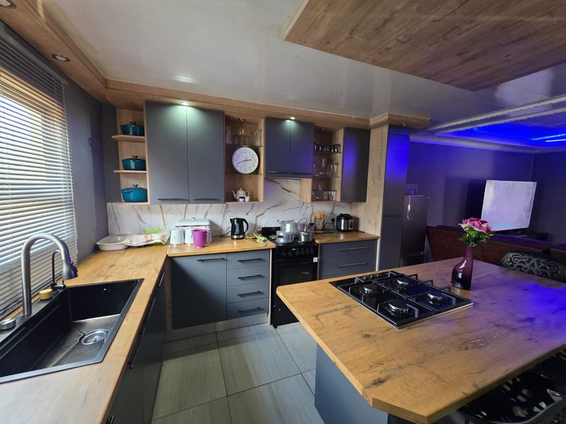 Modern open-plan kitchen featuring dark grey cabinetry, wood-look countertops, integrated gas hob, and contemporary finishes with recessed lighting.