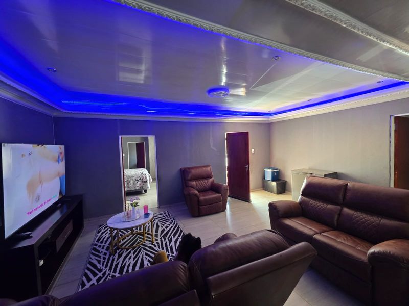 Spacious living room featuring a modern recessed ceiling with integrated blue LED lighting and neutral tiled flooring.