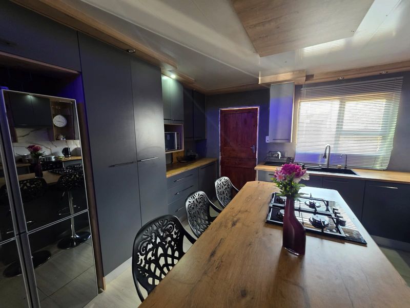 Modern kitchen featuring dark cabinetry, wooden countertops, a central island with a built-in gas hob, and integrated appliances.