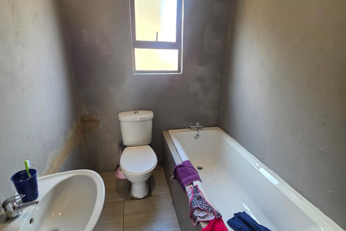 A functional bathroom featuring a pedestal basin, toilet, and bathtub, currently requiring wall finishing and cosmetic updates to complete the space.