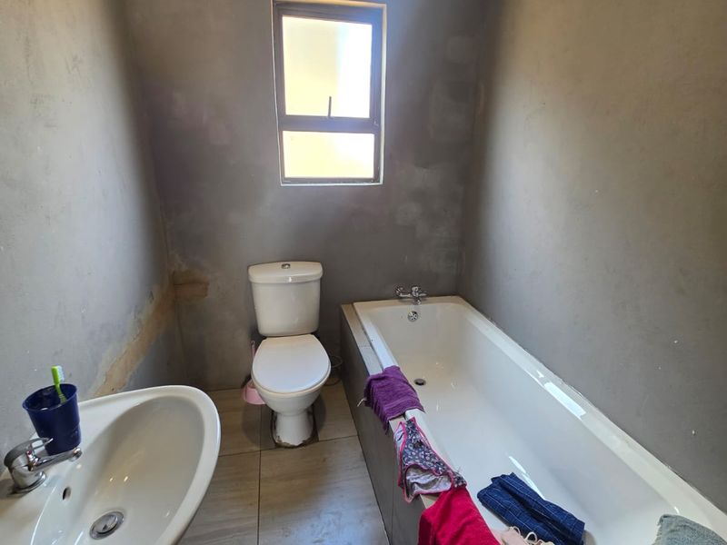A functional bathroom featuring a pedestal basin, toilet, and bathtub, currently requiring wall finishing and cosmetic updates to complete the space.