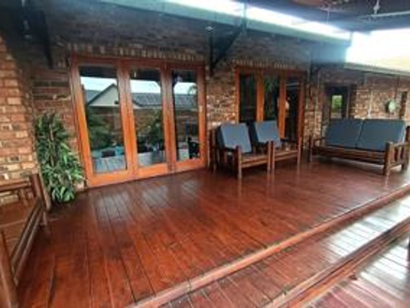 A spacious covered patio featuring timber decking and exposed brick walls, providing seamless indoor-outdoor flow through large timber-framed folding doors.