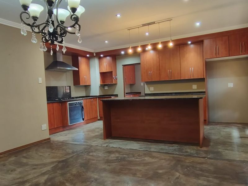 Spacious kitchen featuring warm-toned wooden cabinetry, granite countertops, a central island, and polished concrete flooring, illuminated by recessed lighting and a decorative chandelier.