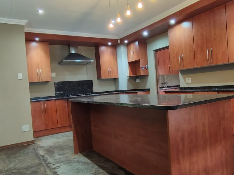 Spacious kitchen featuring wooden cabinetry, granite countertops, a central island, and a stainless steel extractor fan, offering a functional layout for modern living.