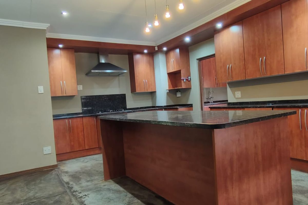 Spacious kitchen featuring wooden cabinetry, granite countertops, a central island, and a stainless steel extractor fan, offering a functional layout for modern living.