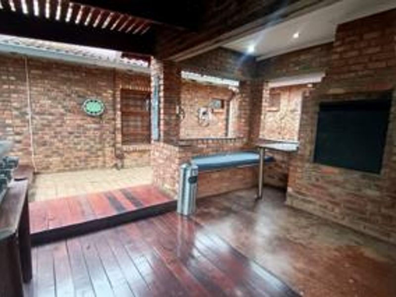 Covered outdoor patio featuring a built-in brick braai, timber decking, and exposed brick walls, ideal for outdoor entertaining.