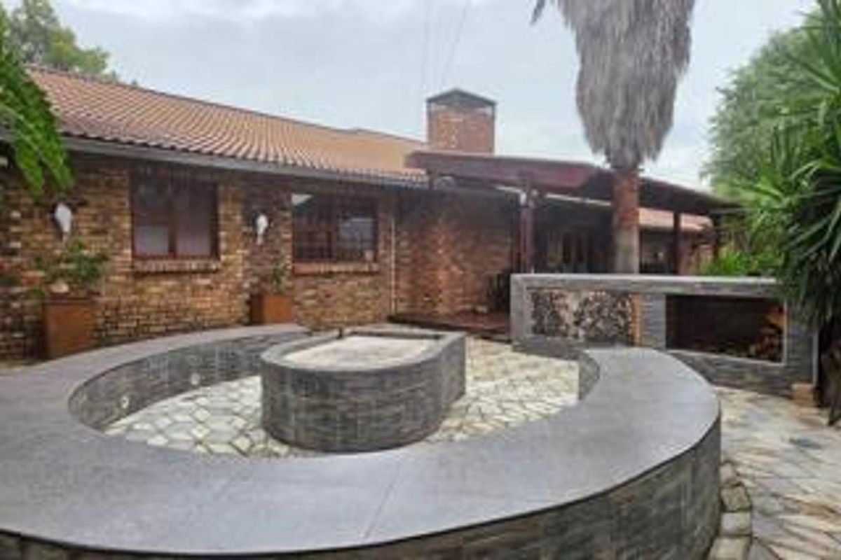 Rear exterior view featuring a brick facade, tiled roof, and a well-designed outdoor entertainment area with a built-in braai and curved stone seating.