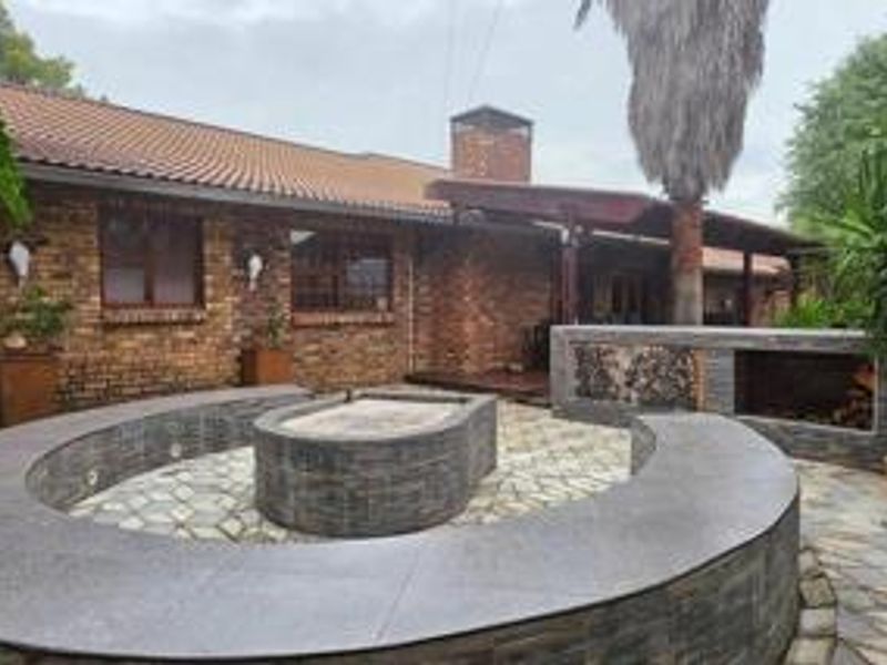 Rear exterior view featuring a brick facade, tiled roof, and a well-designed outdoor entertainment area with a built-in braai and curved stone seating.