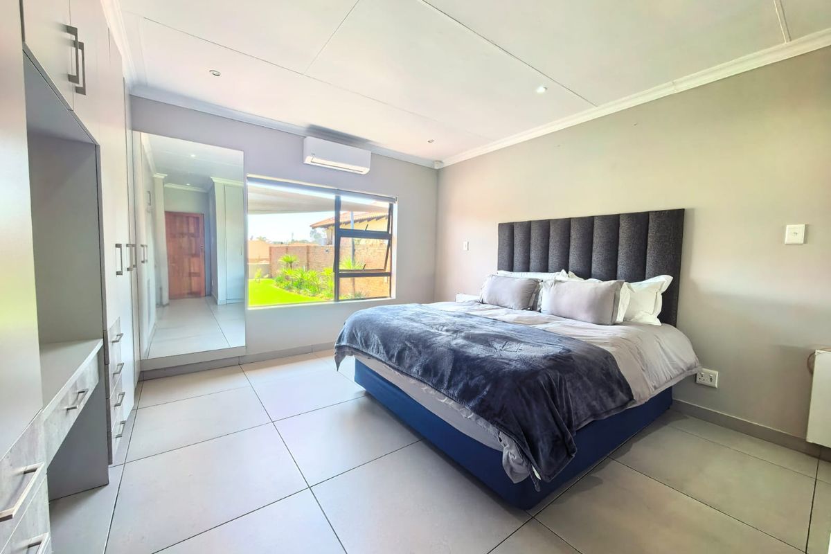 A well-maintained bedroom featuring tiled flooring, built-in cupboards with mirrored doors, and a split-system air conditioner, offering a clean and modern living space.