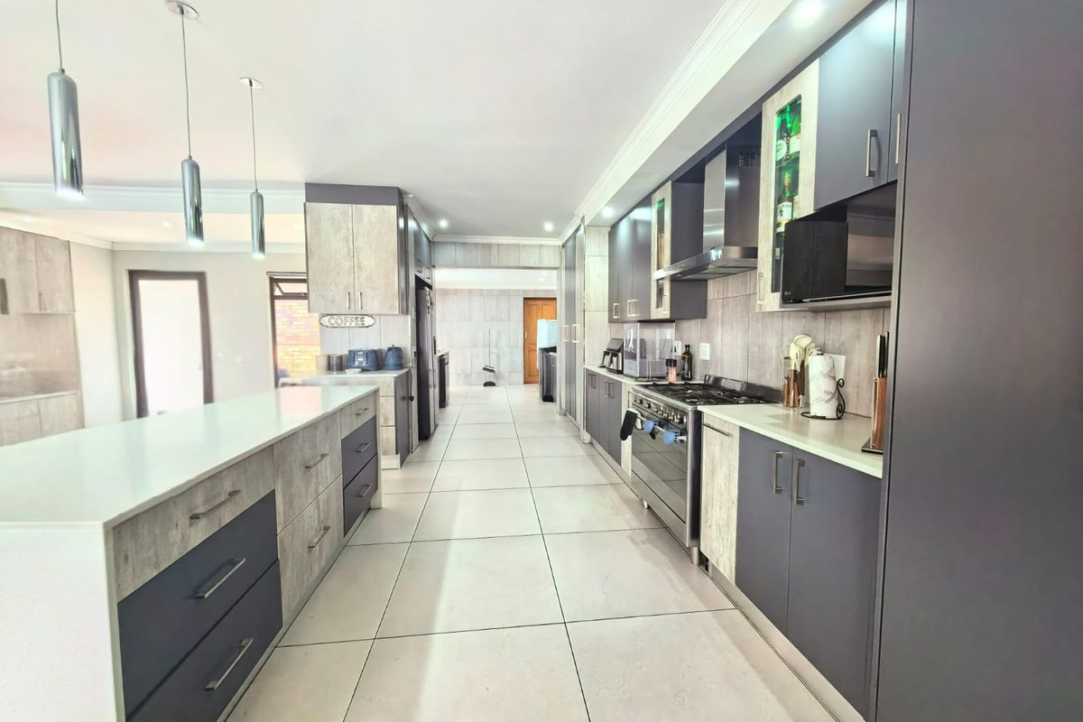 Modern kitchen featuring a large central island, sleek two-tone cabinetry, high-end built-in appliances, and contemporary tiled flooring with ample recessed lighting.