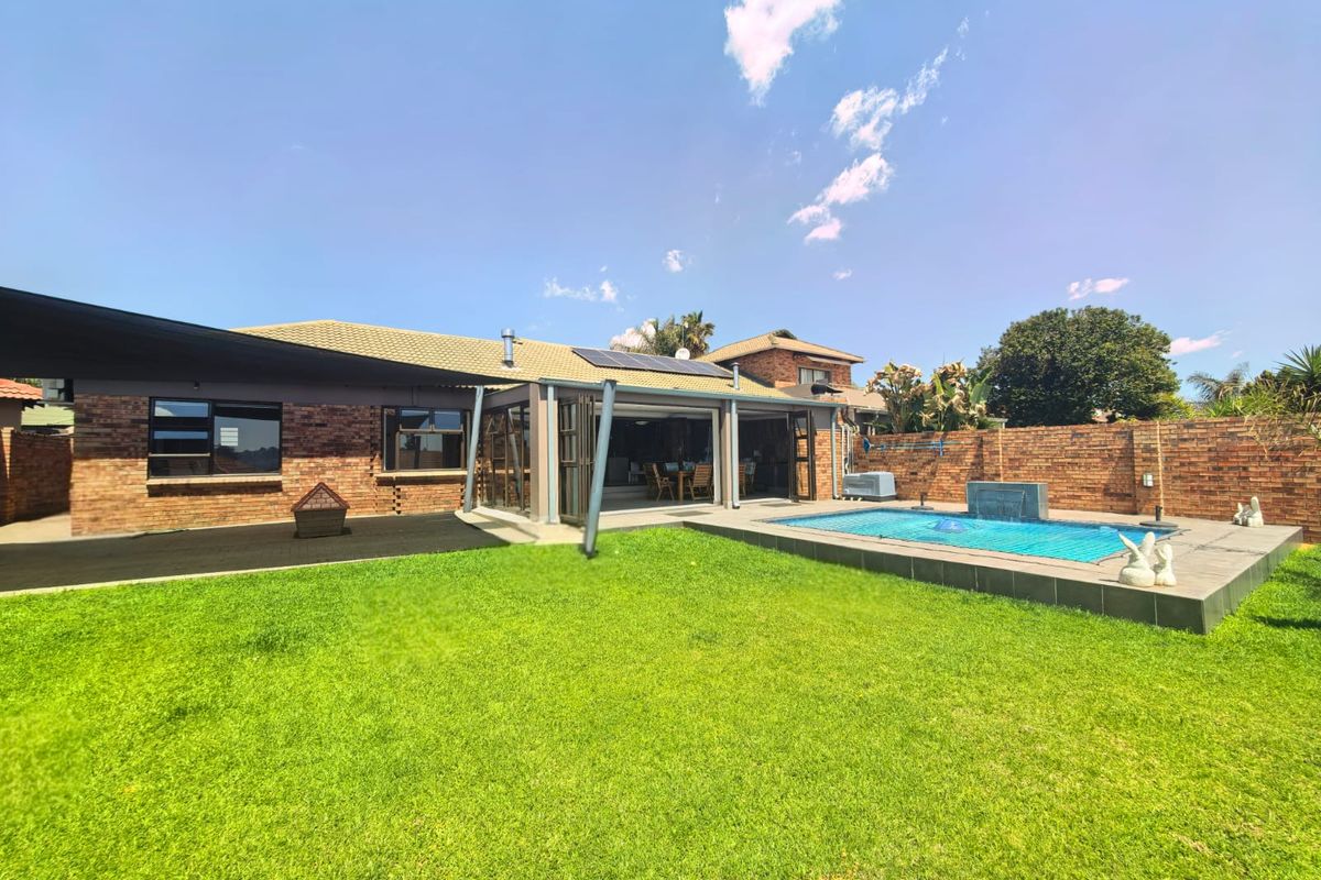 Rear exterior view featuring a well-maintained swimming pool, paved deck, covered patio with stacking doors, and a spacious lawn area.