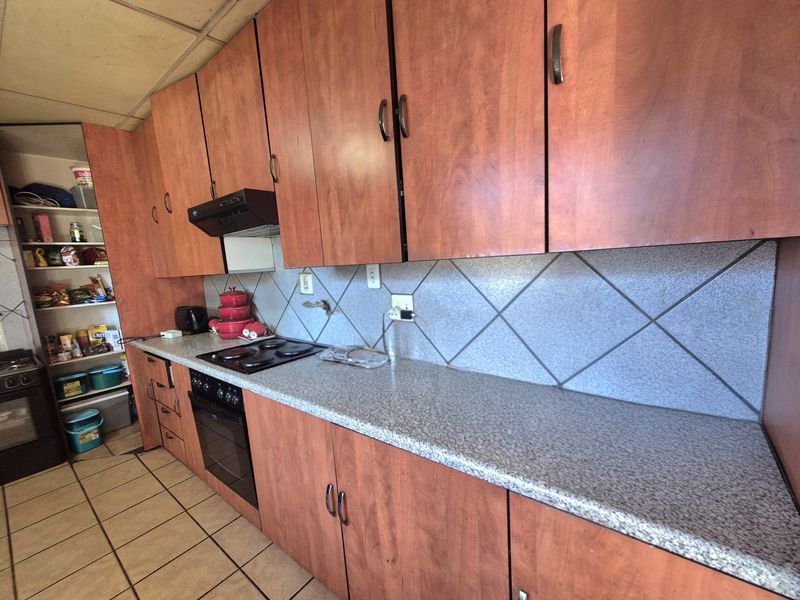 A functional kitchen featuring wood-look laminate cabinetry, a built-in oven with hob, tiled backsplash, and an integrated pantry area.