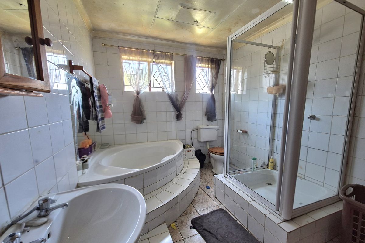 A dated bathroom featuring a built-in corner bathtub, separate shower enclosure, pedestal basin, and toilet, requiring significant renovation and cosmetic updates.