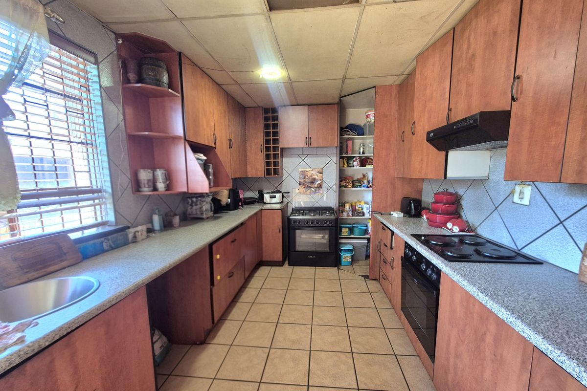 A dated kitchen featuring laminate cabinetry, built-in oven and hob, tiled flooring, and a pantry cupboard, requiring cosmetic updates to modernize the space.