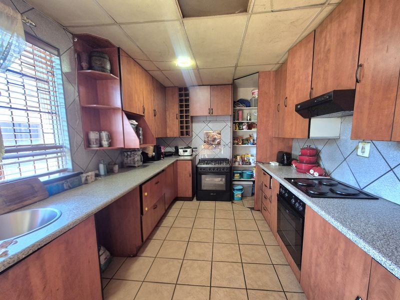 A dated kitchen featuring laminate cabinetry, built-in oven and hob, tiled flooring, and a pantry cupboard, requiring cosmetic updates to modernize the space.