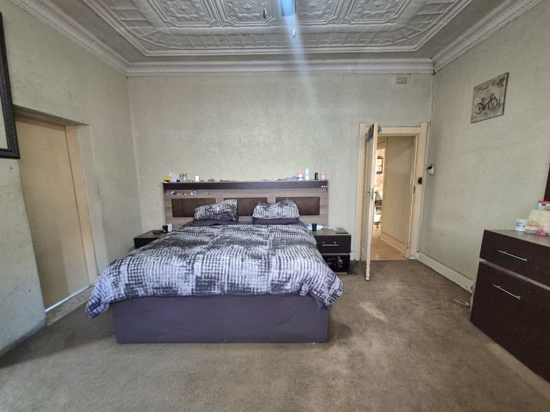 Spacious bedroom featuring an ornate pressed metal ceiling, original cornicing, and a built-in headboard, offering potential for cosmetic renovation.