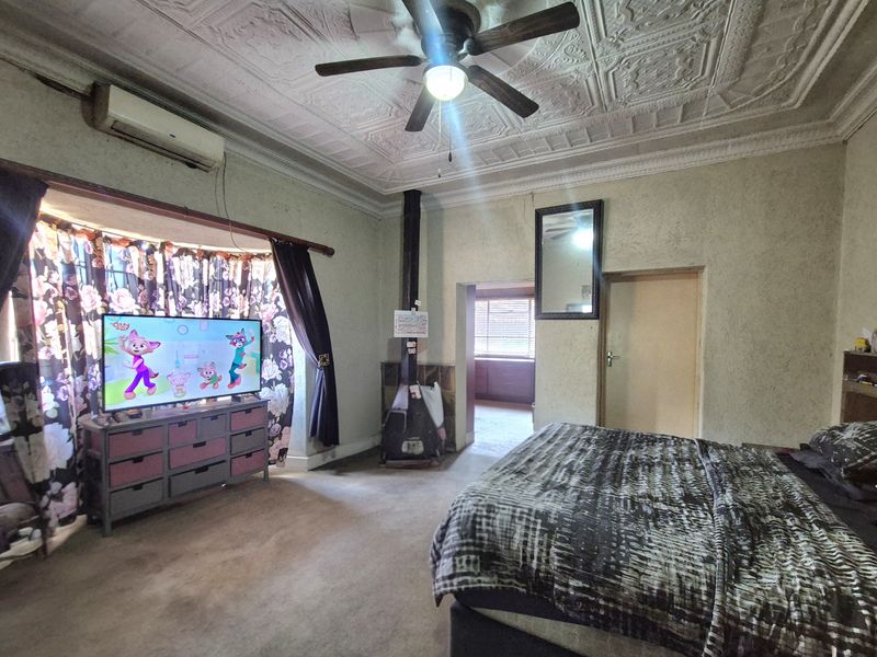 Spacious bedroom featuring a decorative pressed metal ceiling, ceiling fan, wood-burning fireplace, and split-system air conditioning.