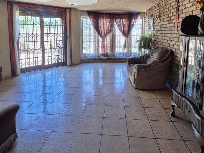 Spacious living room featuring exposed brick walls, ceramic tiled flooring, and large windows with sliding glass doors providing access to the exterior.