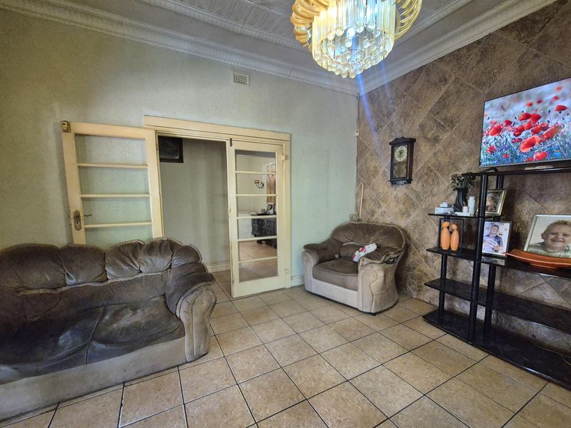 Living room featuring tiled flooring, decorative ceiling, ornate chandelier, and a stone-look feature wall with double french door access to adjacent space.