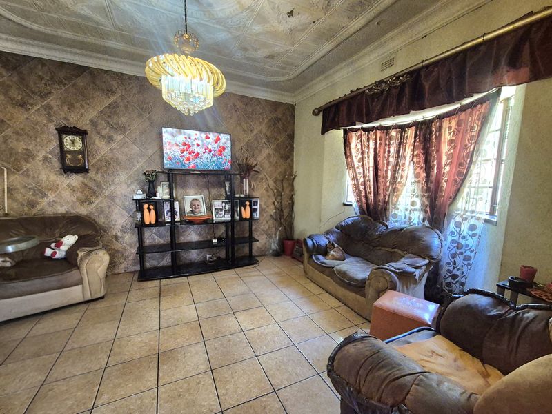 Living room featuring tiled flooring, a decorative pressed metal ceiling, and a tiled feature wall, offering a dated aesthetic ready for modernization.