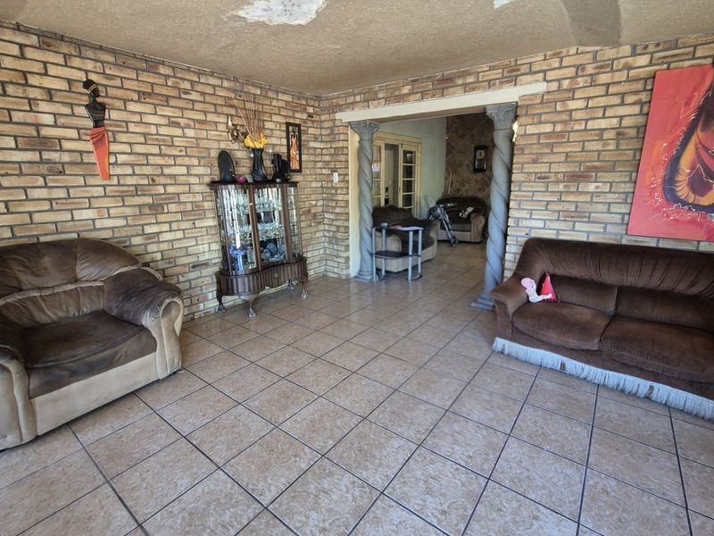 Spacious living area featuring exposed brick walls, ceramic floor tiling, and decorative columns, with visible ceiling damage requiring repair.