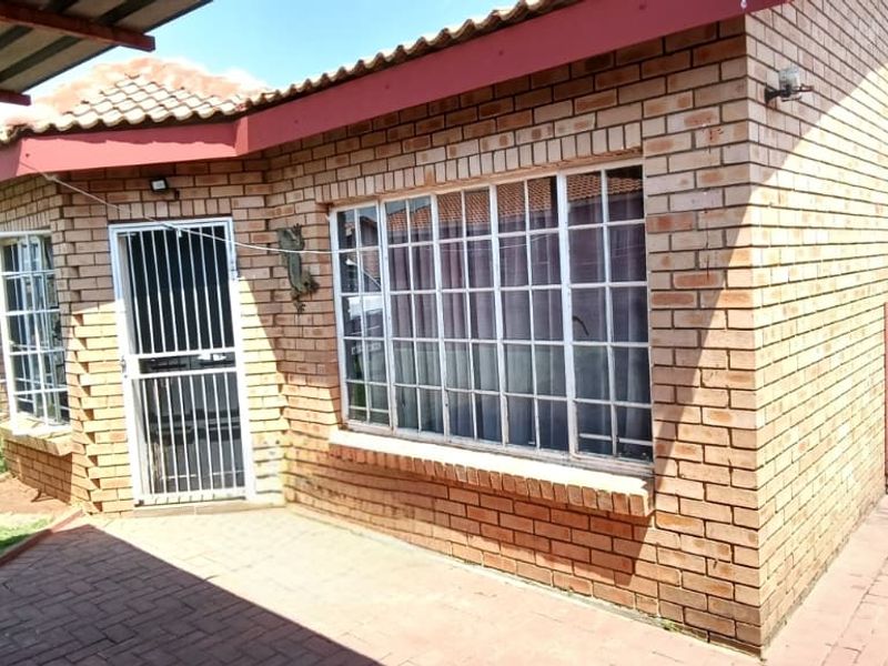 Front exterior view of a face brick townhouse featuring a paved driveway, covered patio area, and secure window bars.