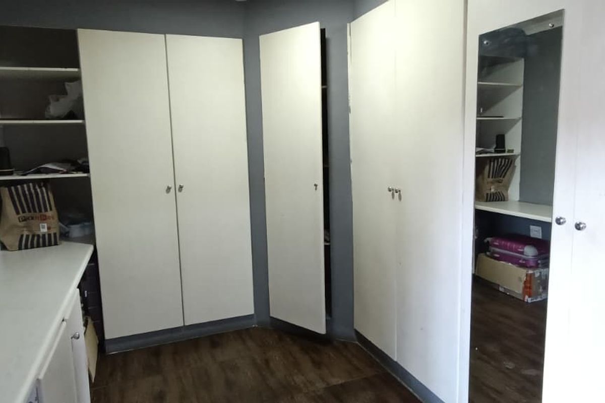 Bedroom featuring extensive built-in cupboard storage, laminate flooring, and integrated shelving units, offering practical storage solutions within the living space.