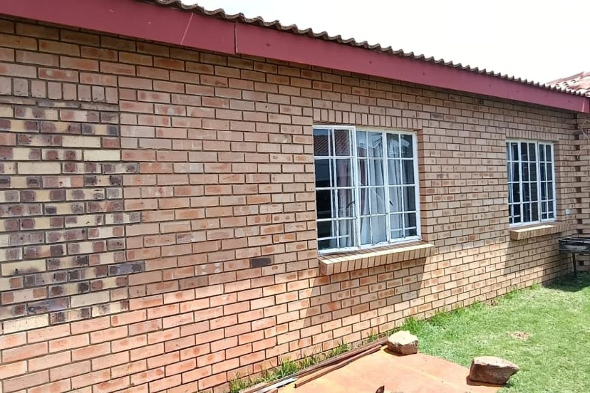 Rear exterior view of the townhouse featuring face brick walls, tiled roofing, and security-fitted windows with visible brickwork inconsistencies.