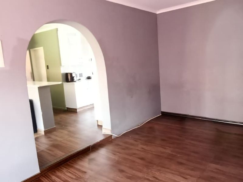 An empty living room featuring laminate flooring and a distinctive arched doorway leading to the kitchen area.