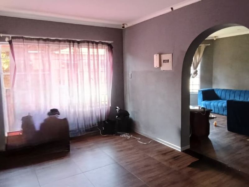 A spacious living area featuring laminate flooring, a distinctive arched doorway, and an exposed electrical distribution board, offering a blank canvas for interior design.