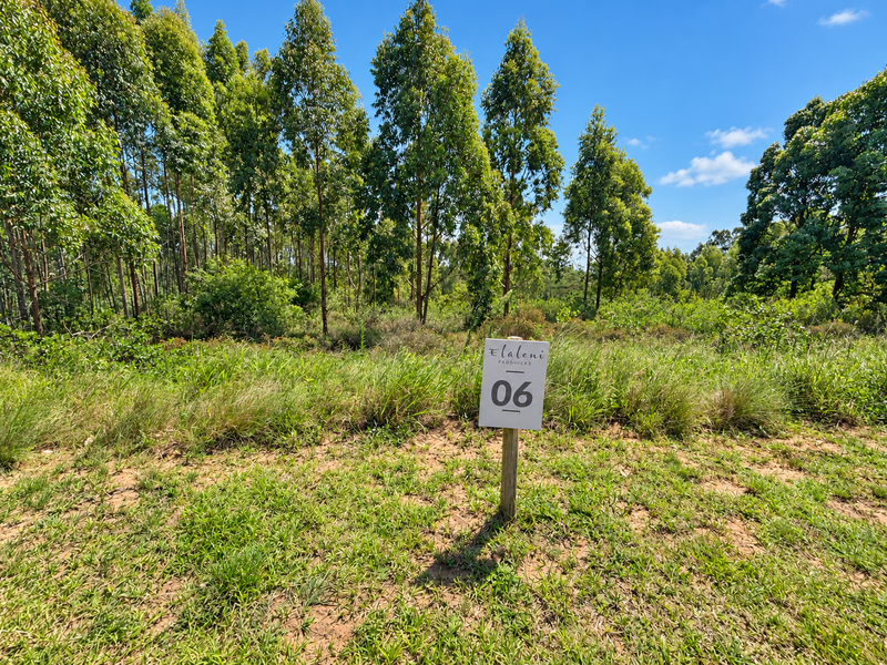 A vacant residential plot featuring natural vegetation and a clear lot marker sign, ready for development in a scenic setting.