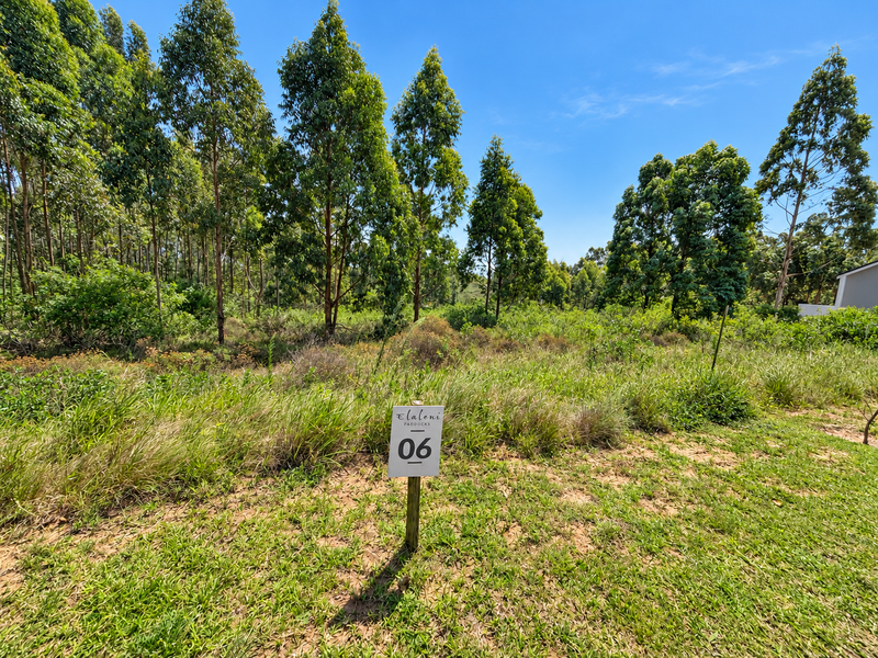A view of a vacant residential plot featuring established trees and natural vegetation, marked with a property identification sign.