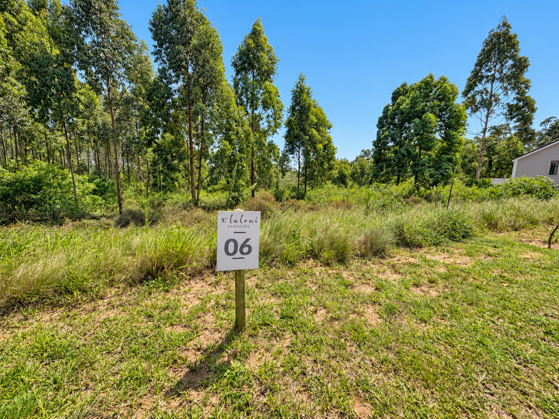A view of a vacant residential plot featuring natural vegetation and mature trees, marked with a property identification sign.