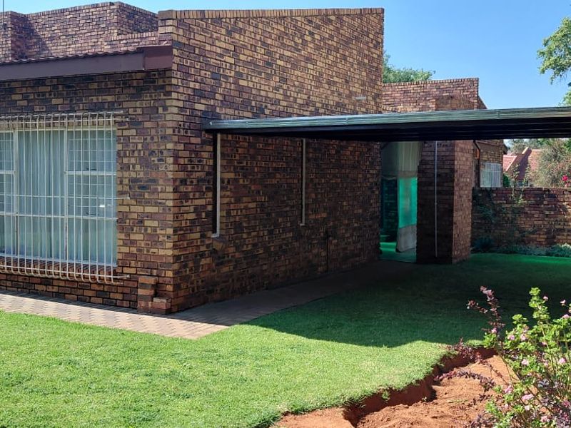 Rear view of a face brick house featuring a covered carport, paved walkway, and established garden area.
