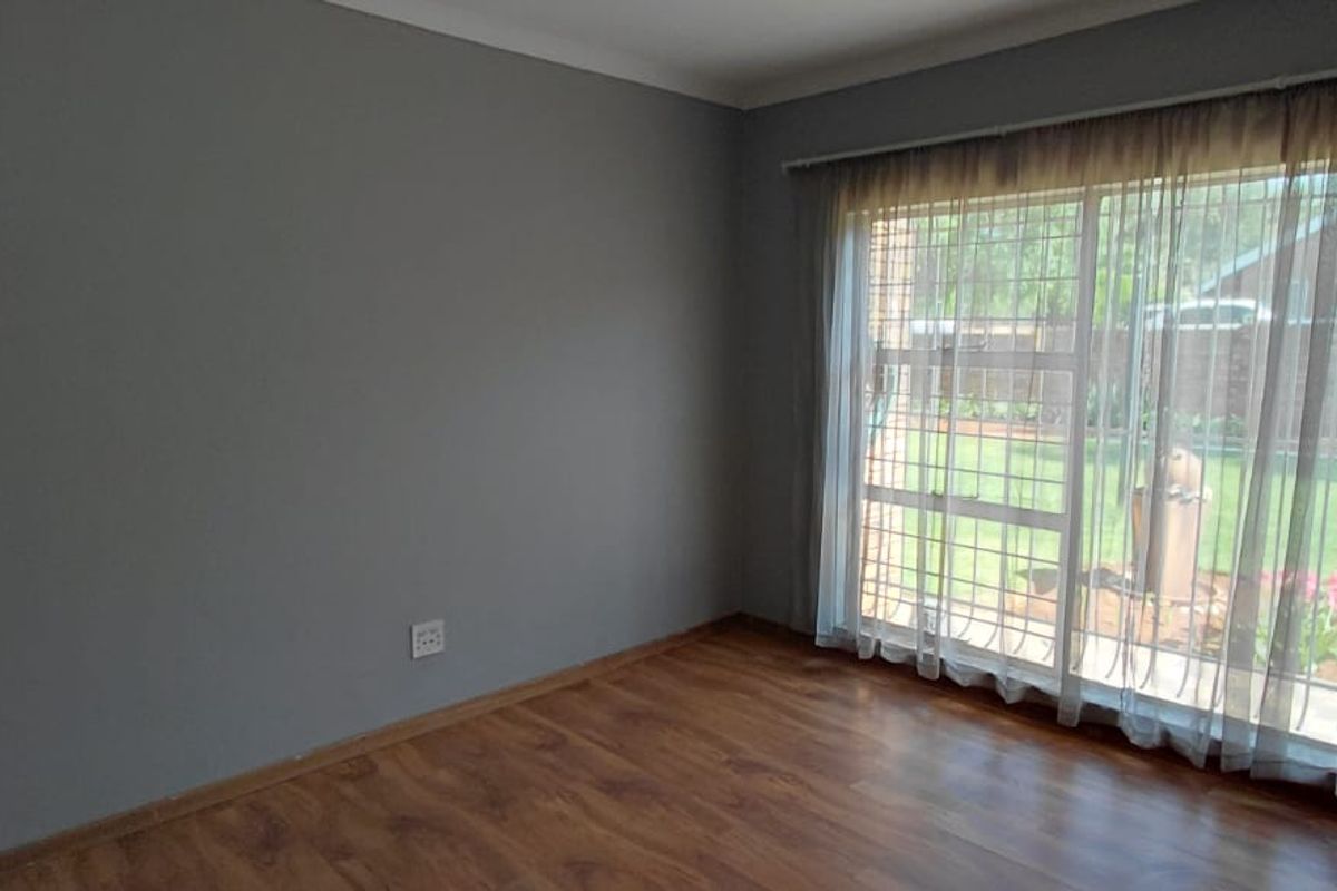 A bright, empty bedroom featuring laminate flooring and a large sliding glass door with security bars, offering views of the garden.