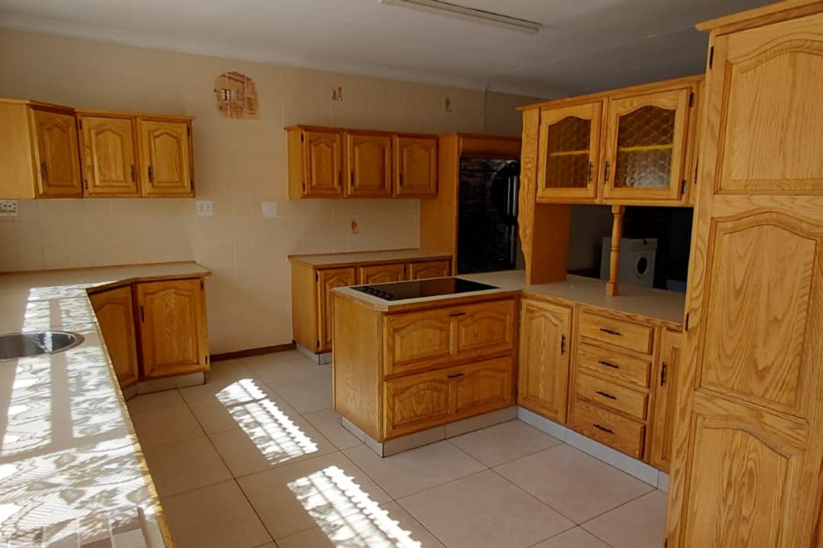 A spacious kitchen featuring extensive wooden cabinetry, a central island with a built-in hob, and tiled flooring throughout.