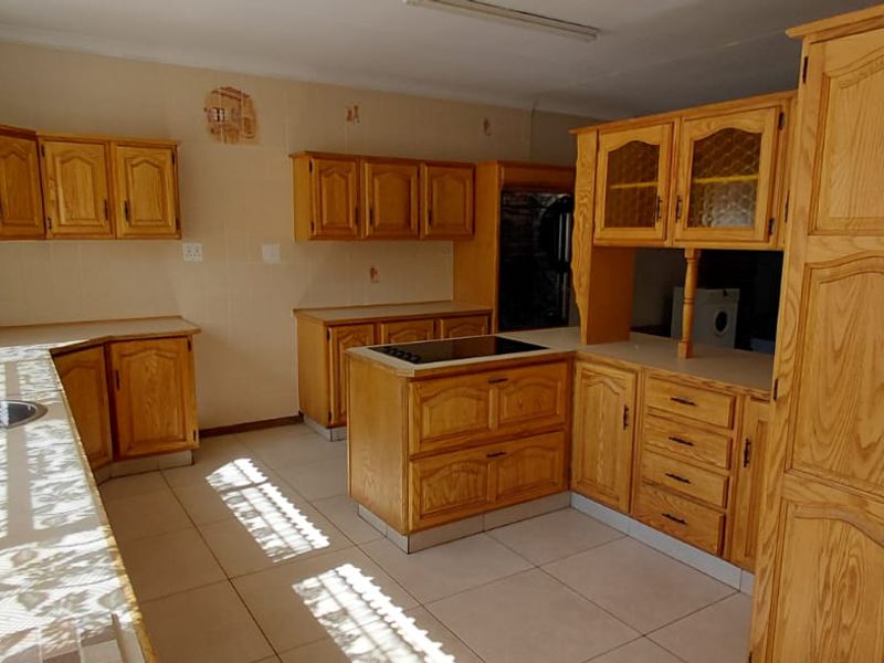 A spacious kitchen featuring extensive wooden cabinetry, a central island with a built-in hob, and tiled flooring throughout.
