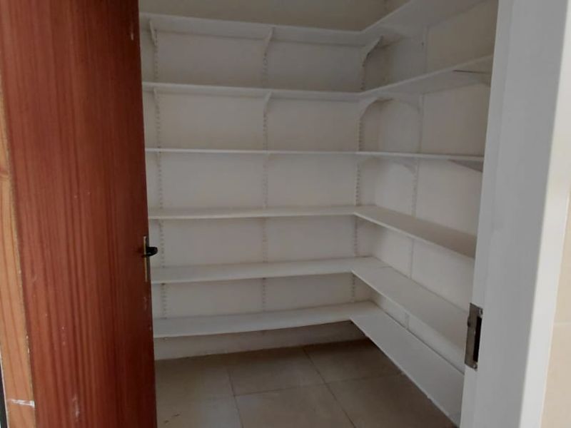 A functional walk-in pantry or scullery area featuring white built-in shelving and tiled flooring, providing ample storage space.