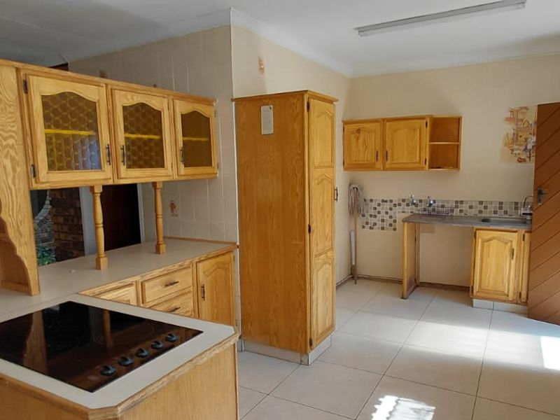 Spacious kitchen featuring extensive wooden cabinetry, built-in electric hob, tiled splashbacks, and a functional layout with ample storage and workspace.