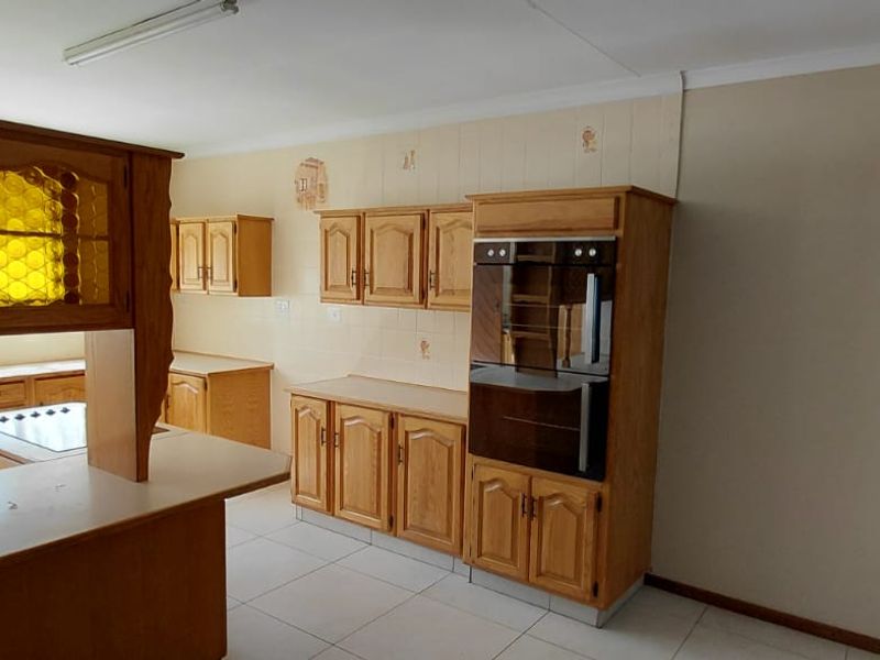 A spacious kitchen featuring traditional wooden cabinetry, built-in oven, hob, and tiled flooring, offering a functional layout with ample storage space.