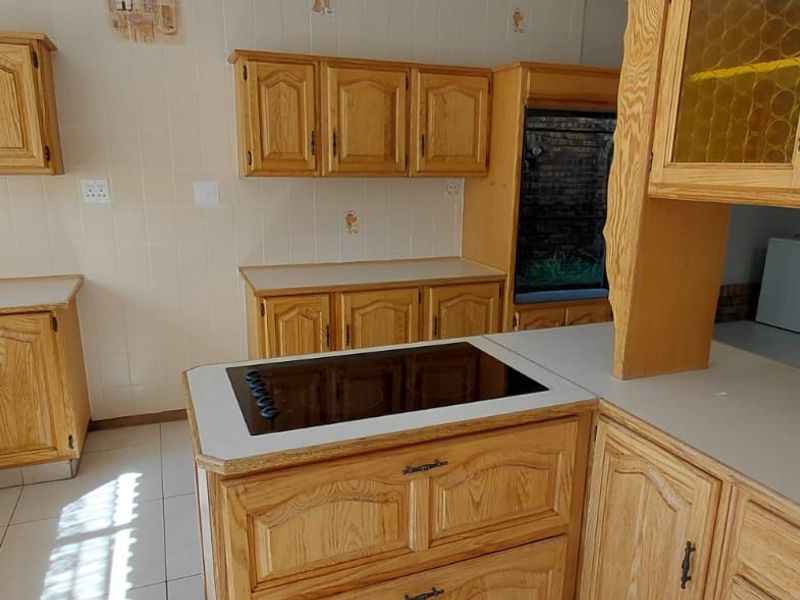 A functional kitchen featuring traditional wooden cabinetry, laminate countertops, and a built-in electric hob, offering a classic layout ready for modernization.