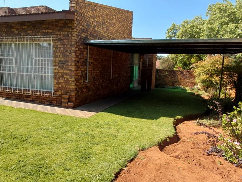 Rear view of the property featuring a face brick facade, a covered carport, paved walkway, and a landscaped garden area.