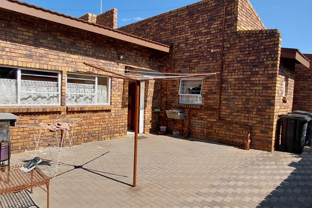 Rear exterior view of a face brick house featuring a paved patio area and an external utility sink.