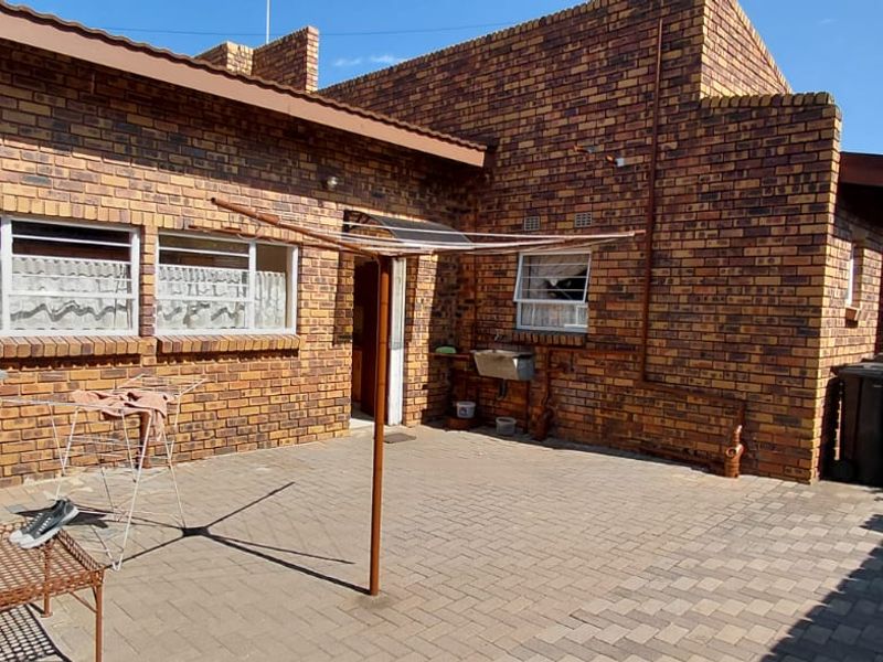 Rear exterior view of a face brick house featuring a paved patio area and an external utility sink.