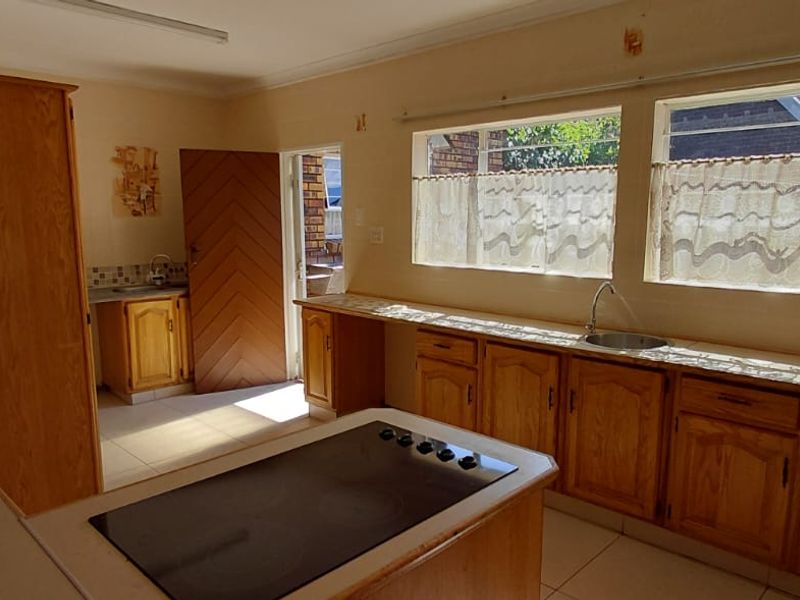 A spacious kitchen featuring extensive wooden cabinetry, a central island with an integrated electric hob, and ample natural light from large windows.