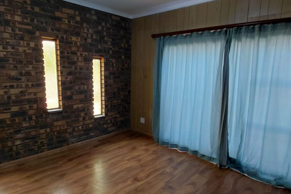 An empty living room featuring a rustic exposed brick wall with vertical windows, wood paneling, and a large sliding door leading to the exterior.