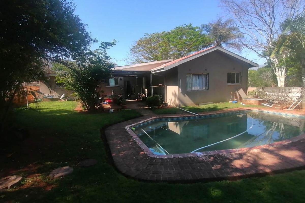 Rear view of the property featuring a swimming pool with brick coping, a covered patio area, and a spacious garden.