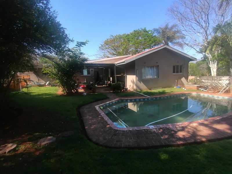 Rear view of the property featuring a swimming pool with brick coping, a covered patio area, and a spacious garden.