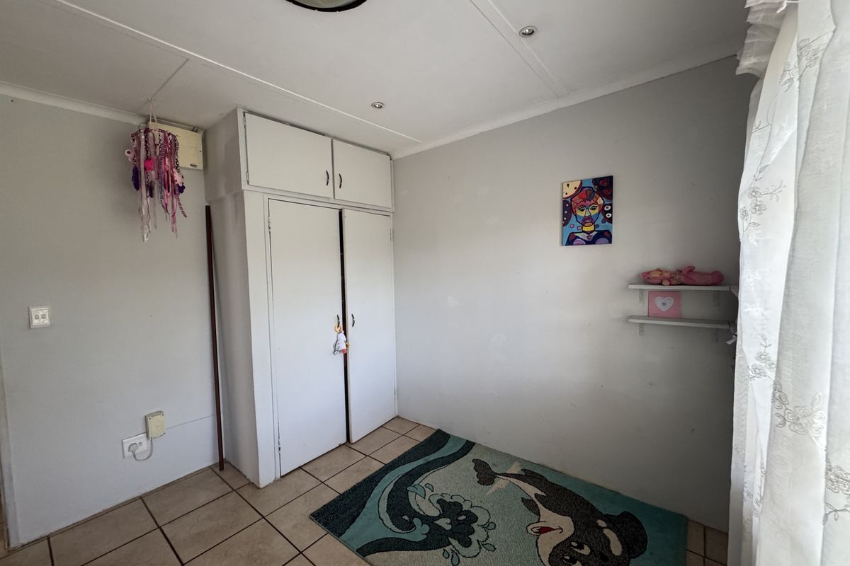 A compact bedroom featuring tiled flooring, a built-in wardrobe with overhead storage, and wall-mounted shelving.