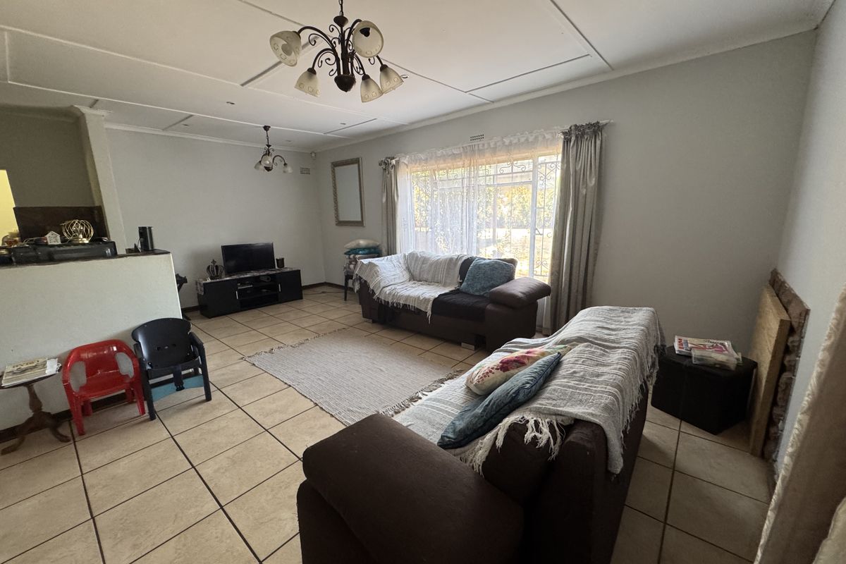 Spacious living room featuring ceramic floor tiles, a large window with security bars, and decorative ceiling lighting.